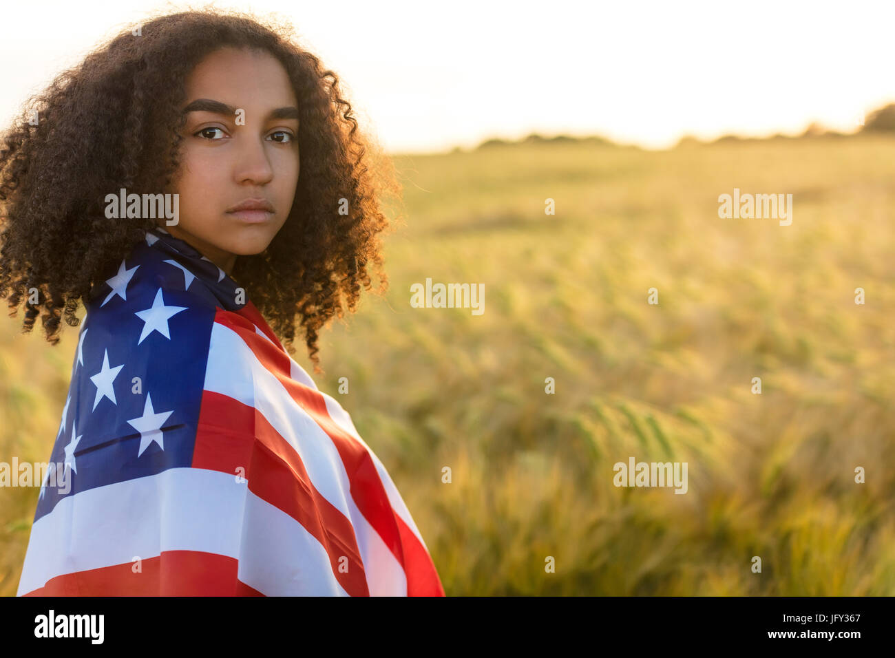 Sad depressed mixed race African American girl teenager female young woman with tears in her eyes in a field of wheat or barley crops holding and wrap Stock Photo
