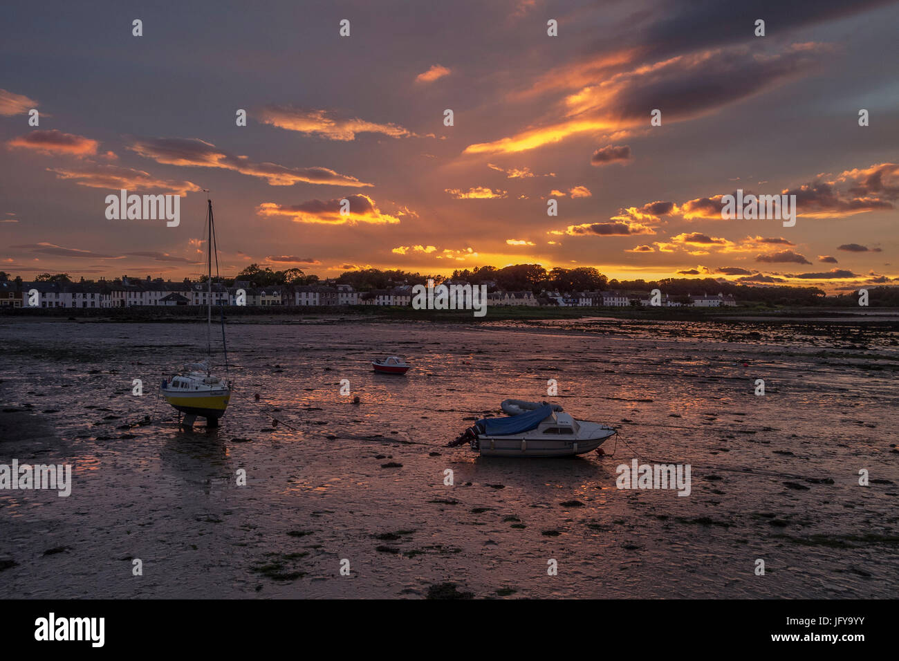 Small boats high and dry on the mud in Garlieston harbour at sunset with the tide out.(landscape format) Stock Photo