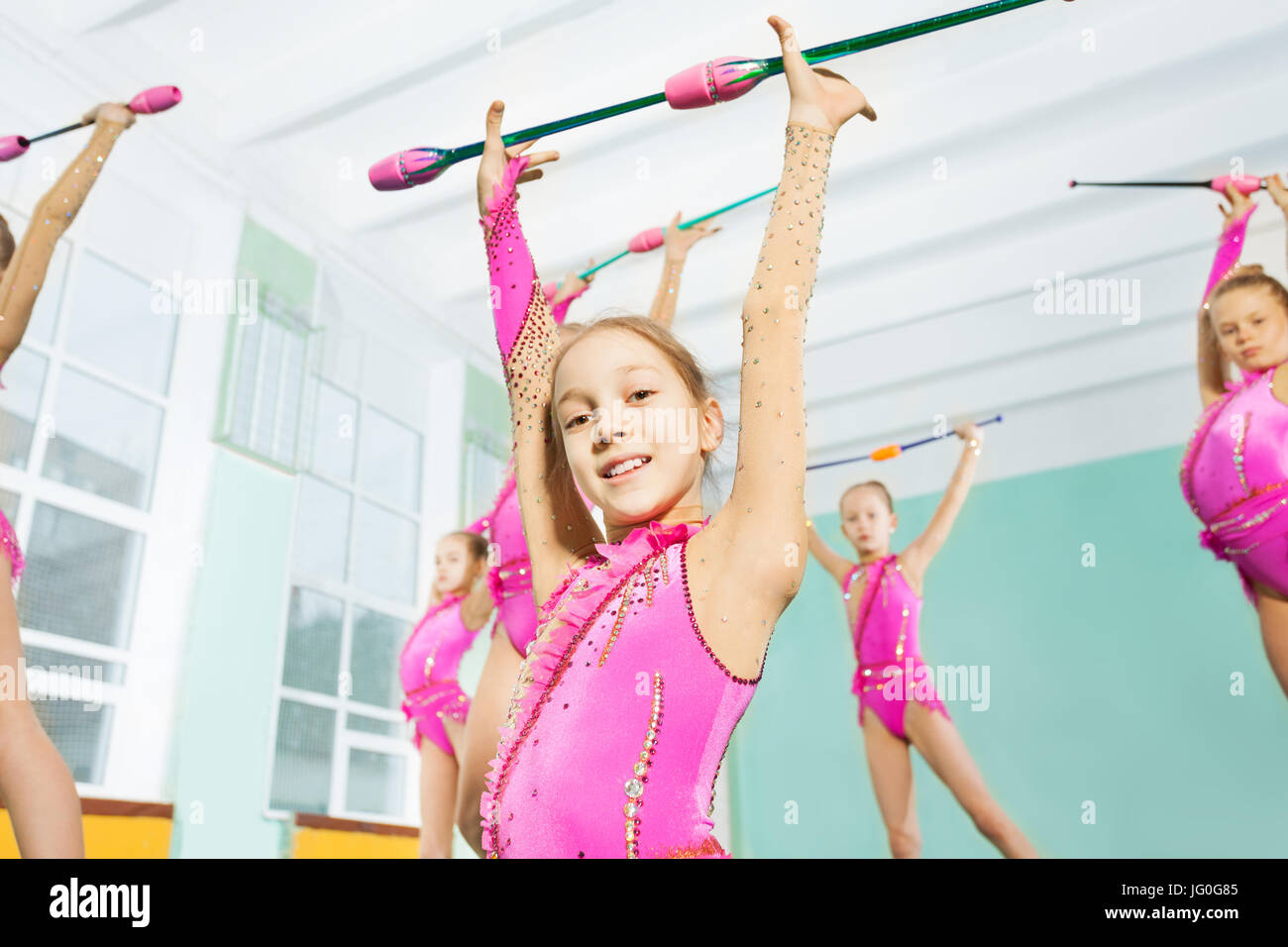 Close-up portrait of happy 11 years old girl wearing pink leotard, doing gymnastic exercises with clubs in sports hall Stock Photo