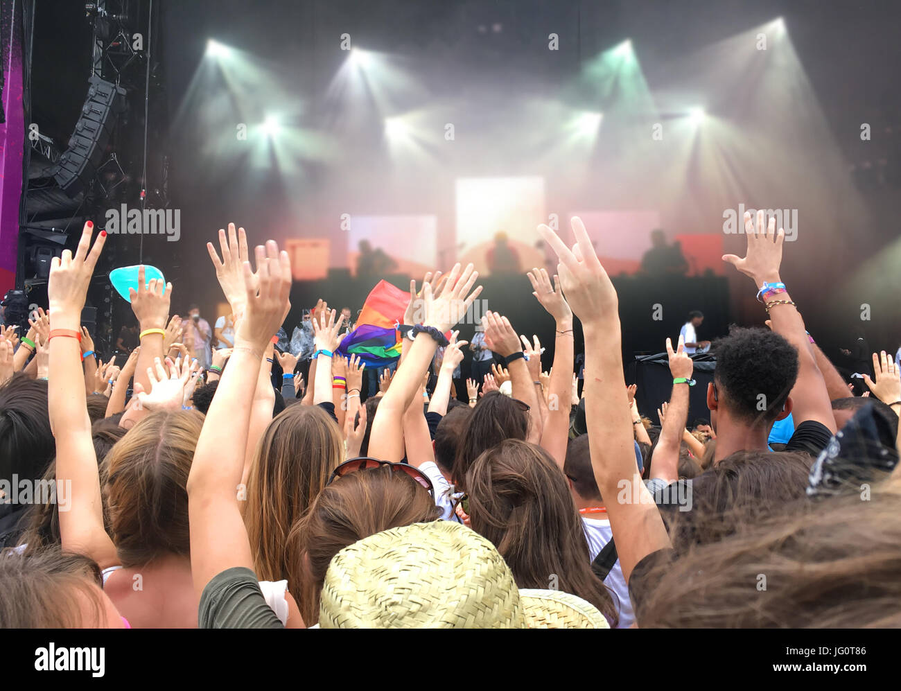Audience with hands raised at a music festival, blurred stage lights in the background Stock Photo