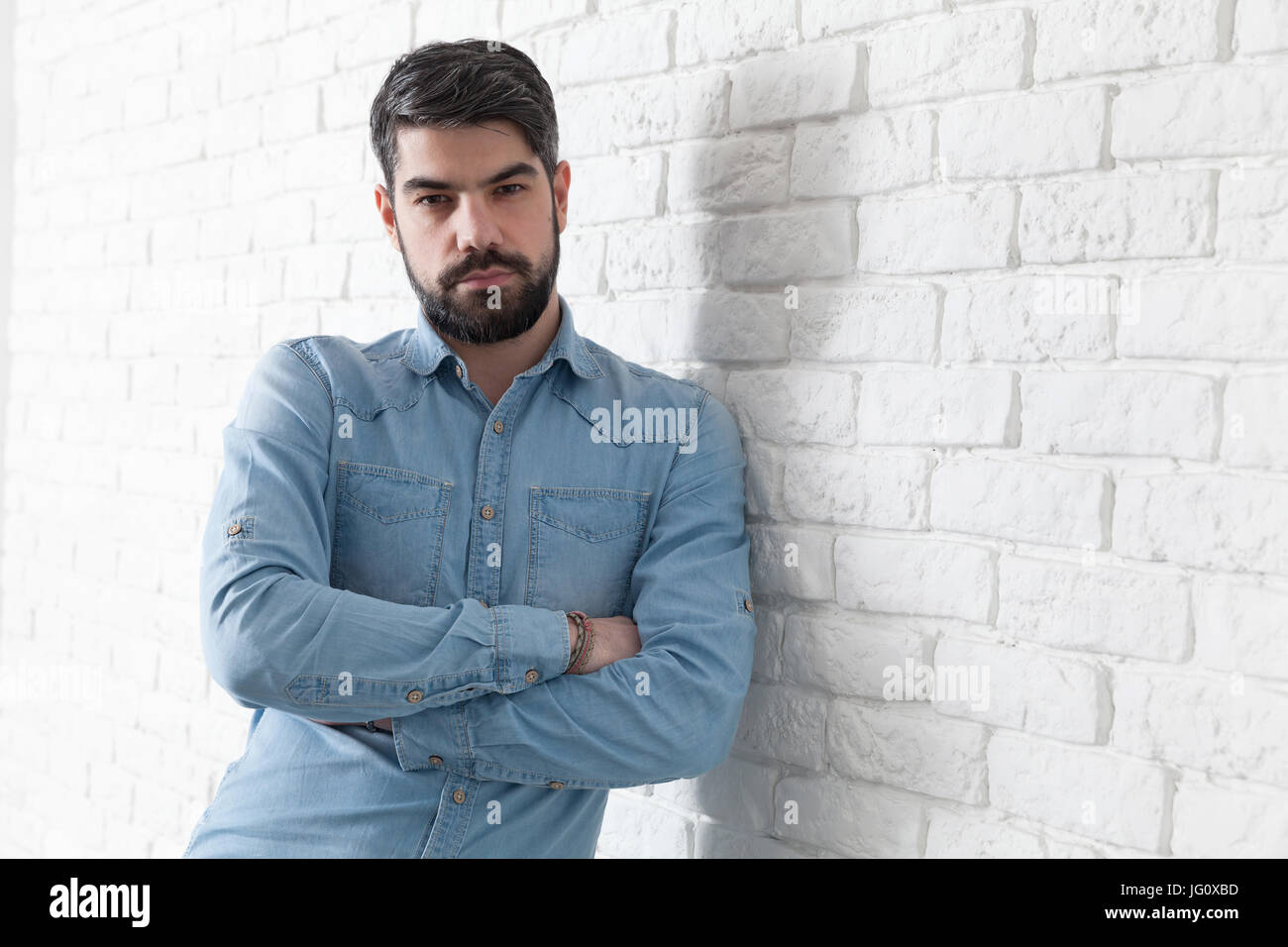 Handsome man leaning against a white brick wall Stock Photo - Alamy