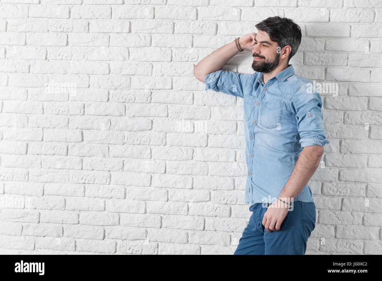Handsome man leaning against a white brick wall Stock Photo - Alamy