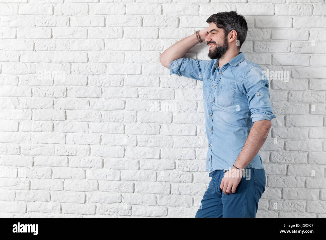 Handsome man leaning against a white brick wall Stock Photo - Alamy