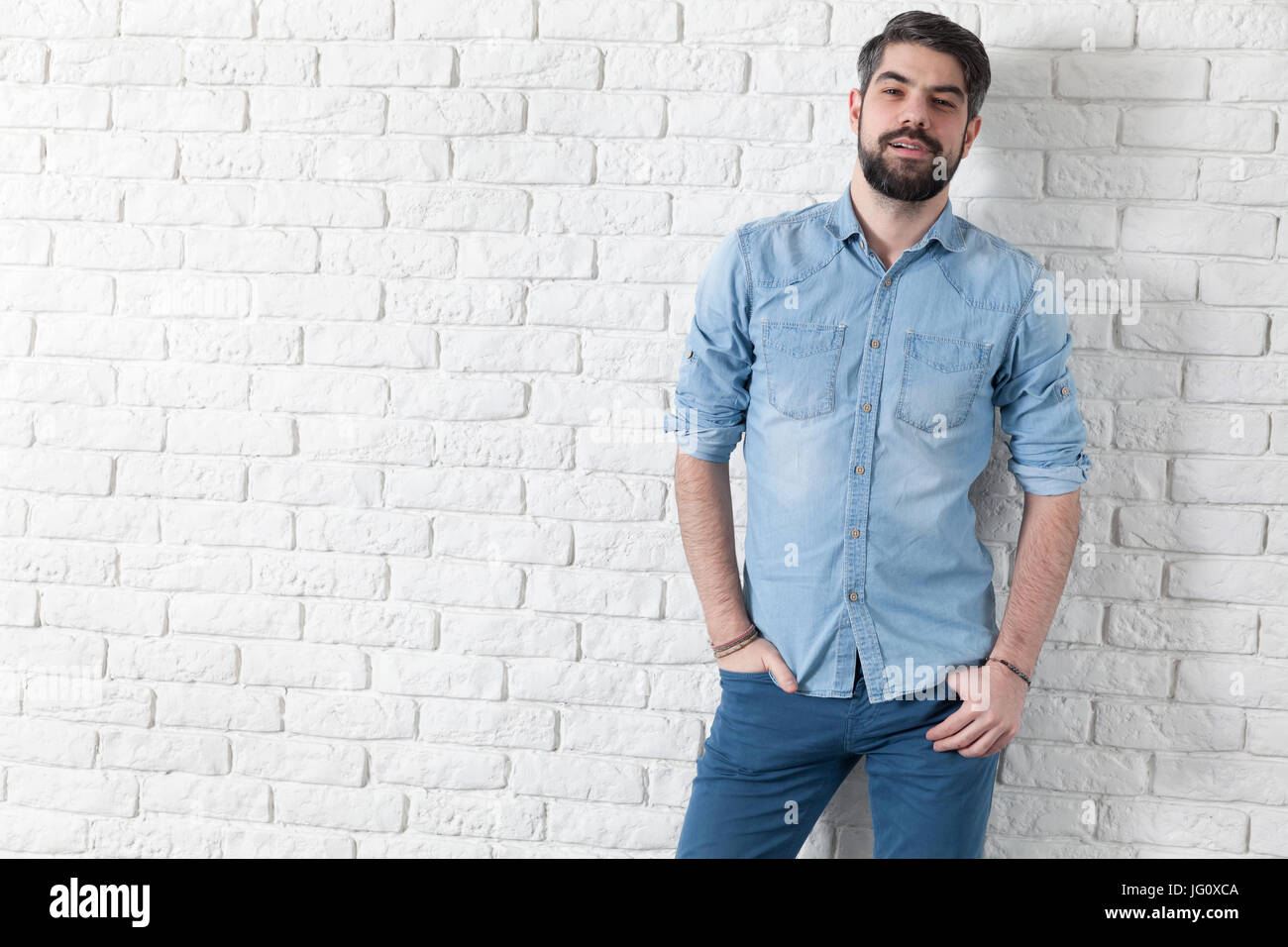 Handsome man leaning against a white brick wall Stock Photo - Alamy