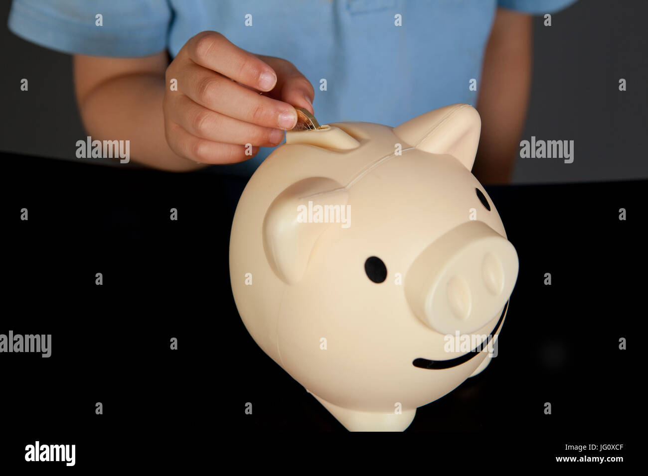 a boy in school uniform putting money in his piggy bank Stock Photo - Alamy