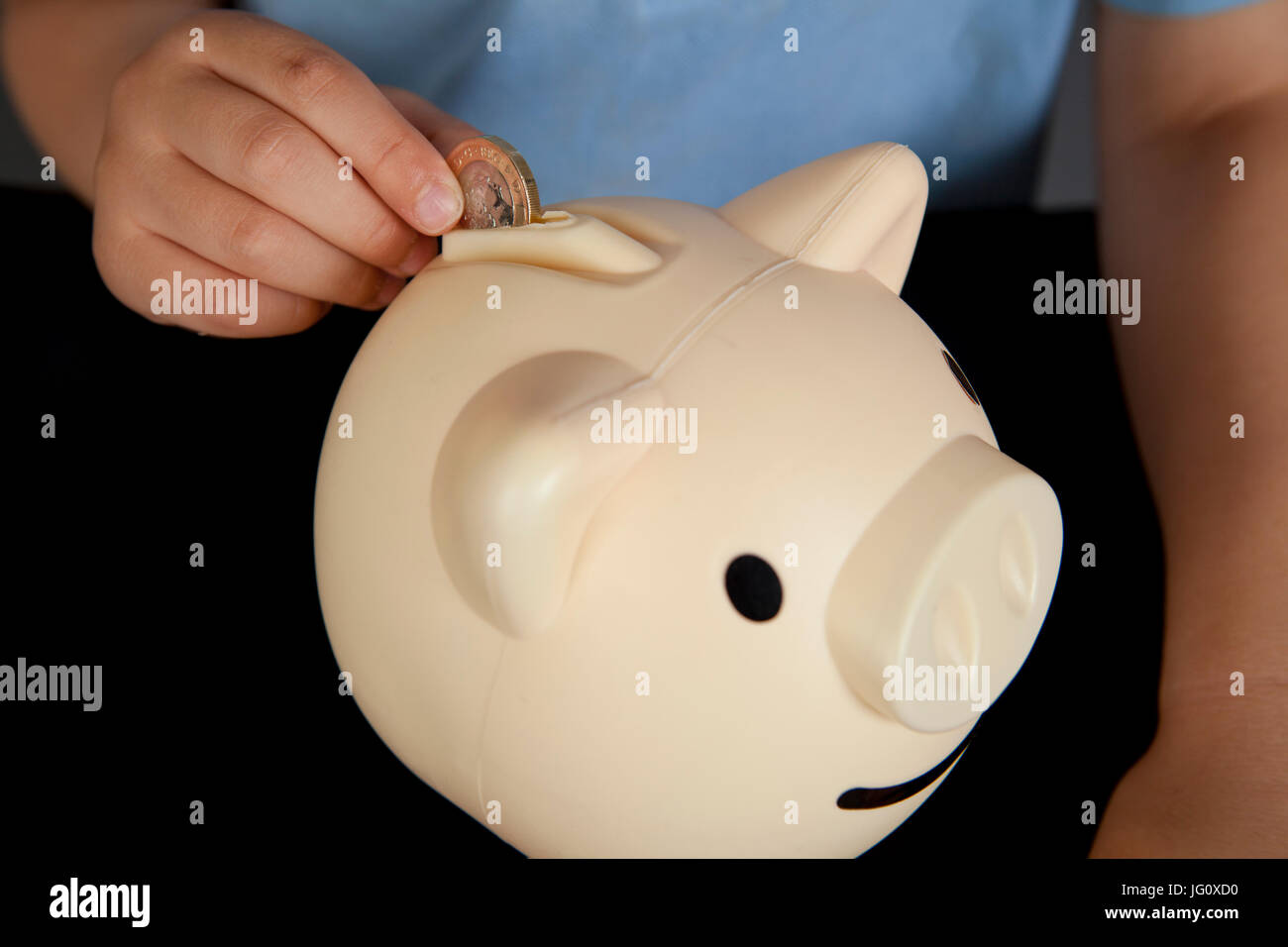 a boy in school uniform putting money in his piggy bank Stock Photo - Alamy