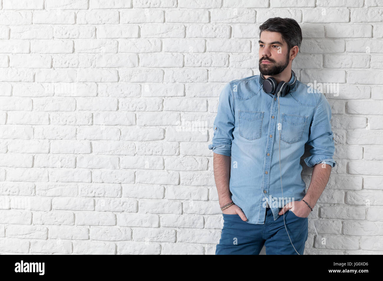 Handsome man leaning against a white brick wall Stock Photo - Alamy