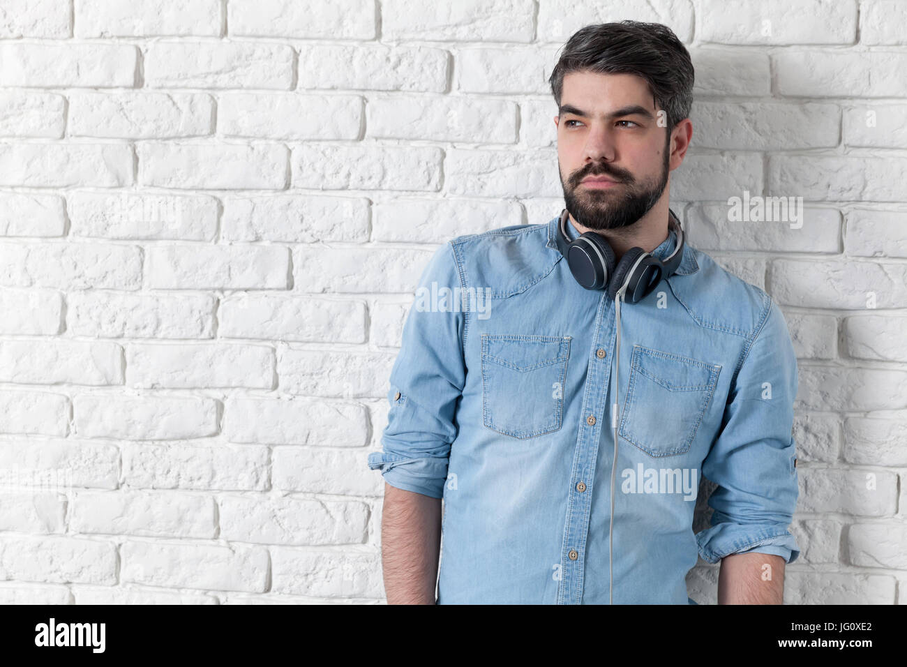Handsome man leaning against a white brick wall Stock Photo - Alamy