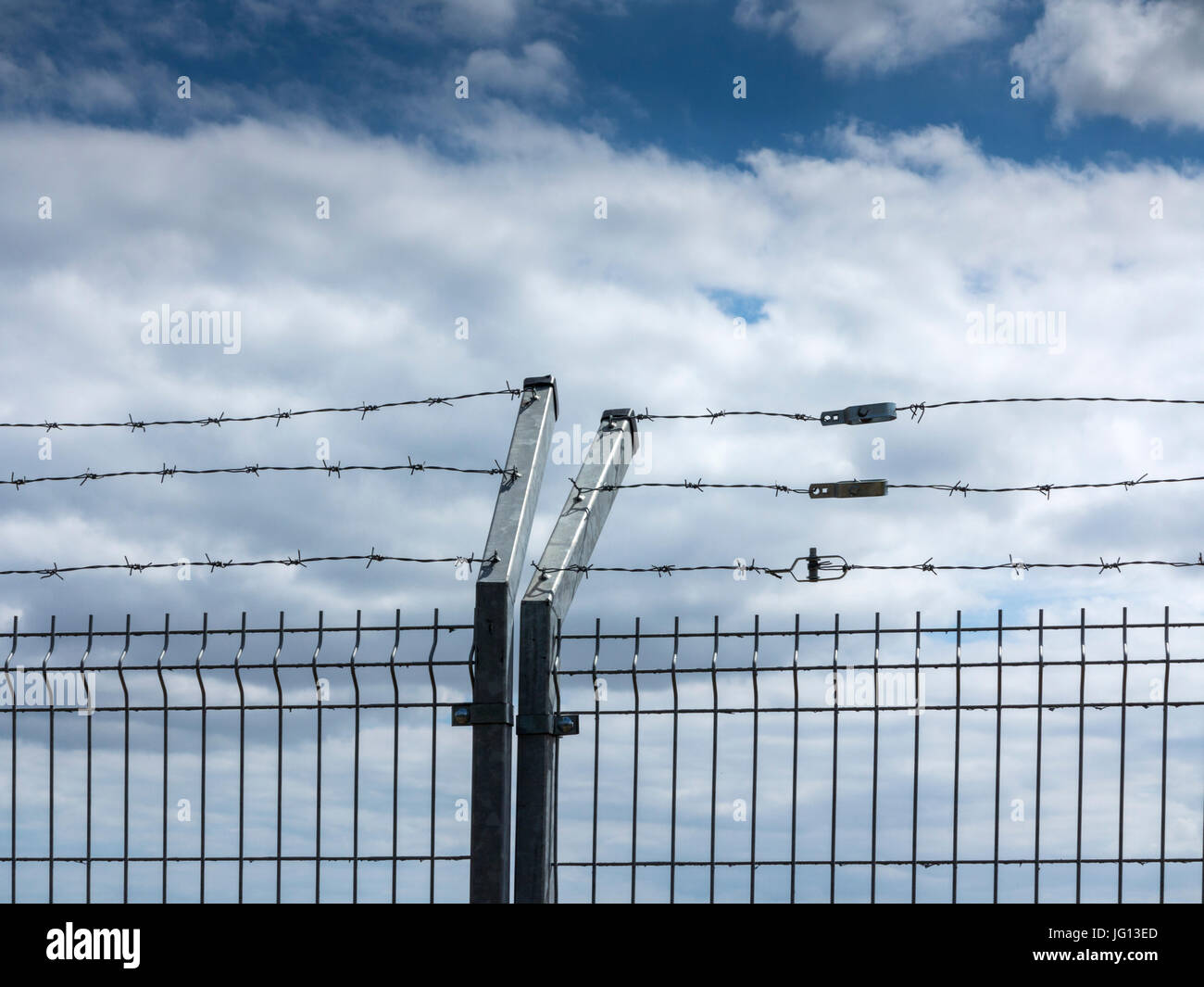 Security fencing against a blue and cloudy sky Stock Photo - Alamy