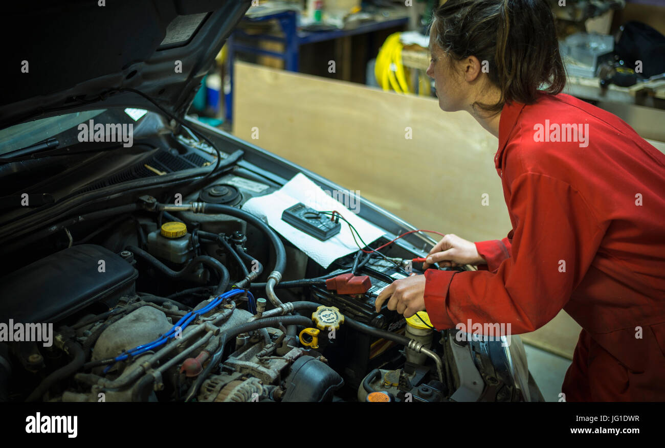 Female mechanic testing car battery with multimeter tool. Stock Photo