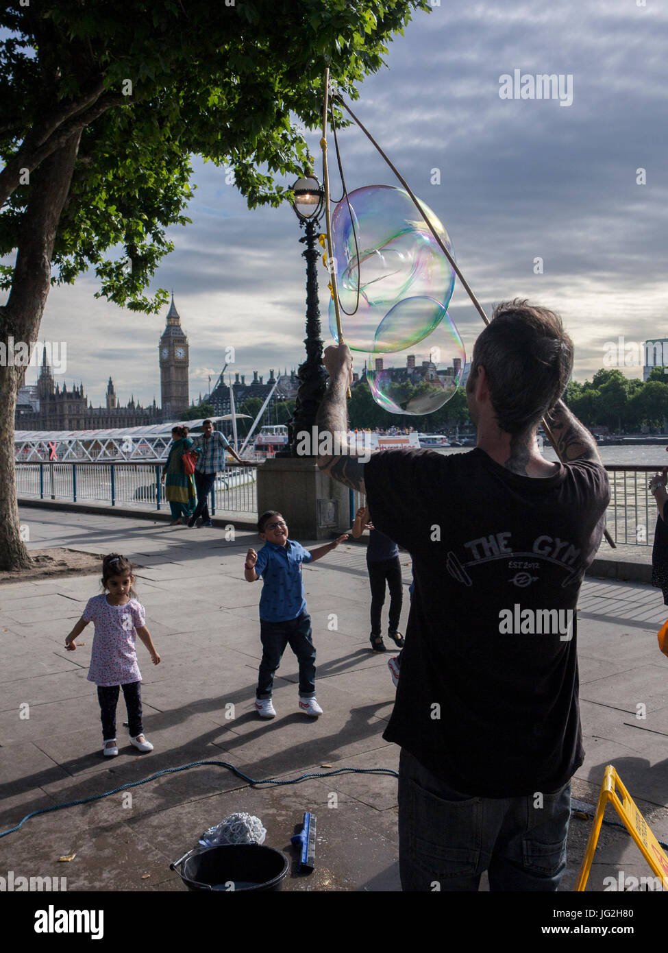 A street busker blows bubbles on the South Bank of the River Thames in London with the Houses of Parliament and Big ben in the background Stock Photo