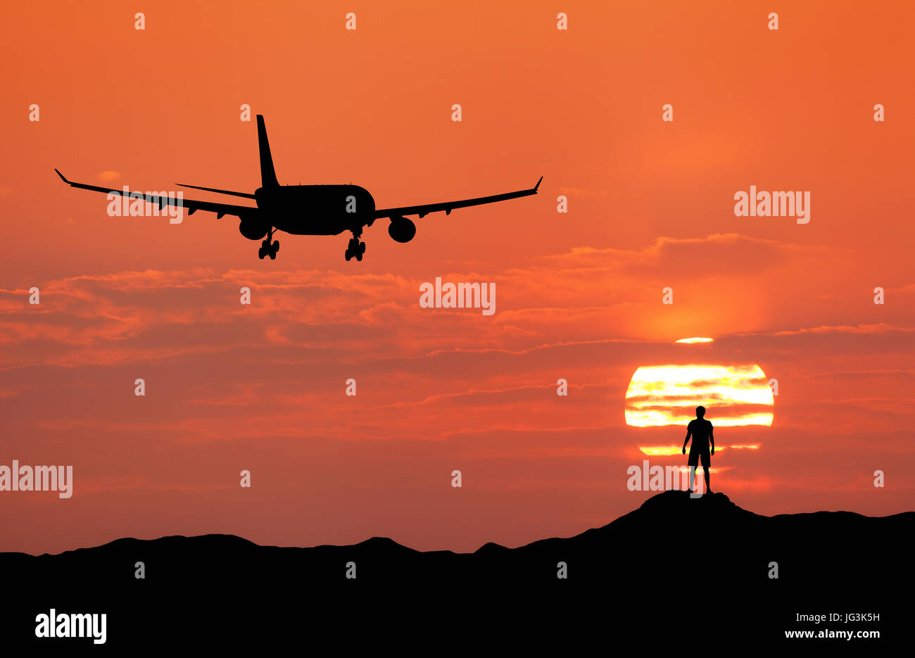 Airplane and silhouette of a standing happy man on the hill at sunset. Summer landscape with landing passenger airplane. Plane flying in the red sky w Stock Photo
