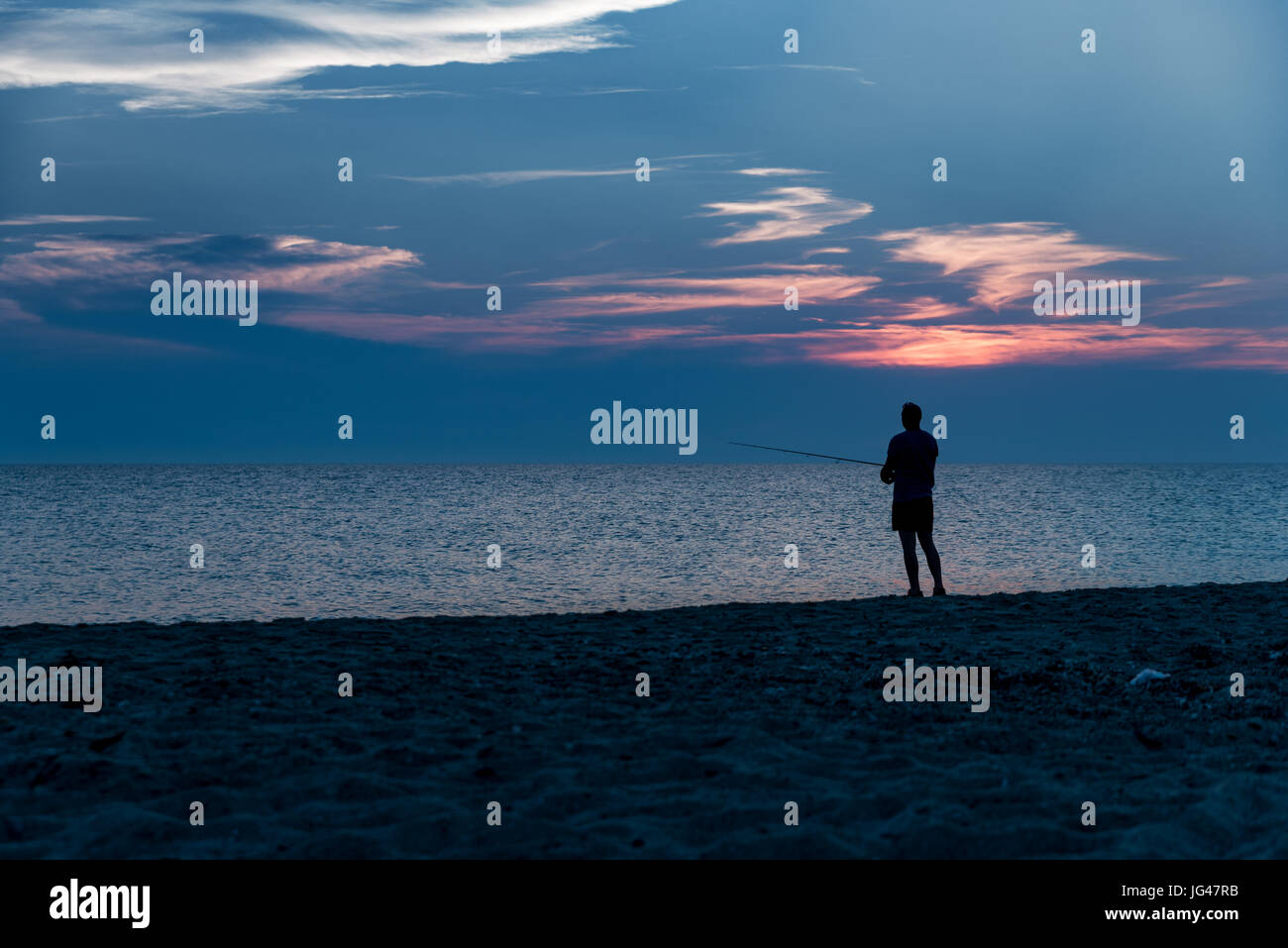 Angler on the beach by the ocean when sun is setting Stock Photo - Alamy