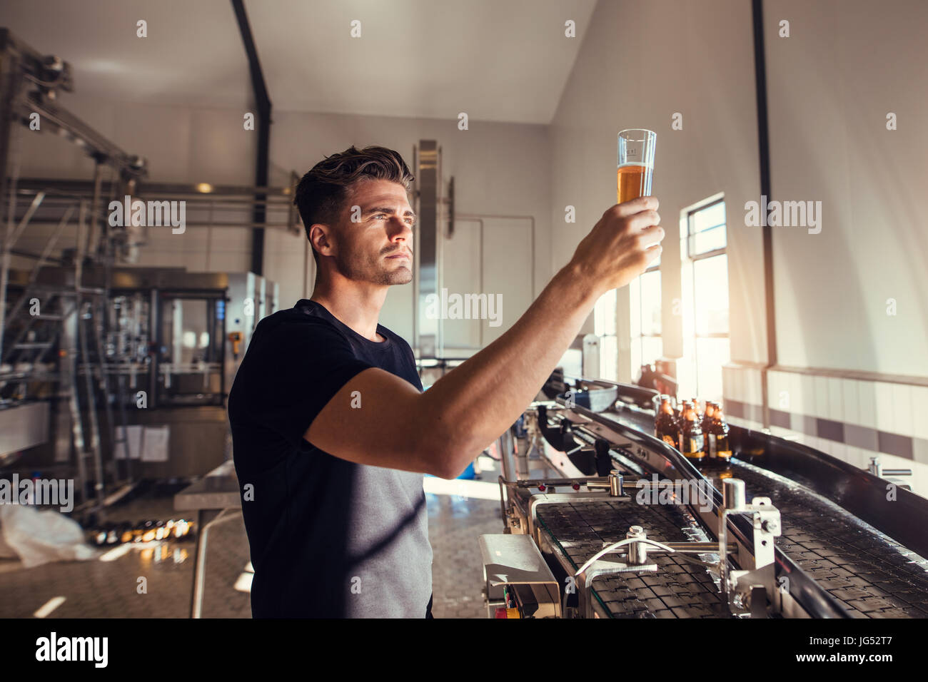 Young man examining the quality of craft beer at brewery. Male inspector working at alcohol manufacturing factory checking the beer. Stock Photo