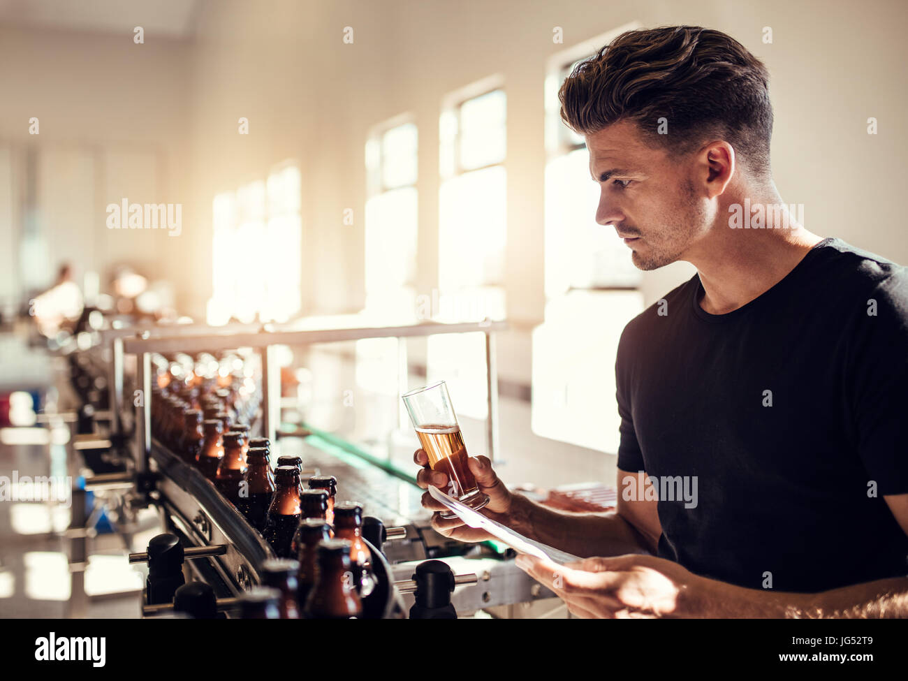 Young man examining the quality of beer at brewery. Male inspector working at alcohol manufacturing factory checking the craft beer. Stock Photo