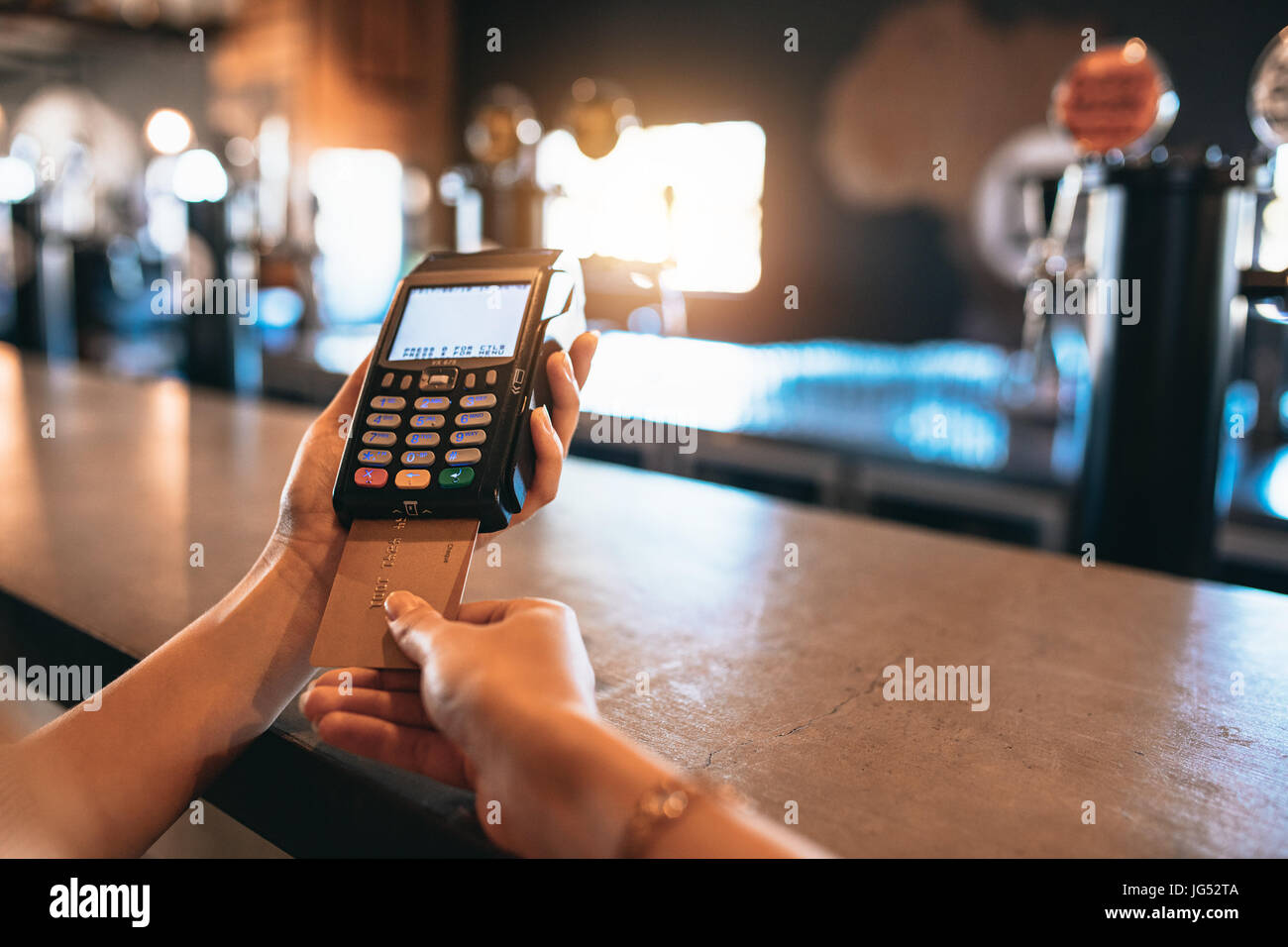 Hands of woman paying bill using a credit card at bar. Cropped shot of female at brewery factory doing cashless payment. Stock Photo