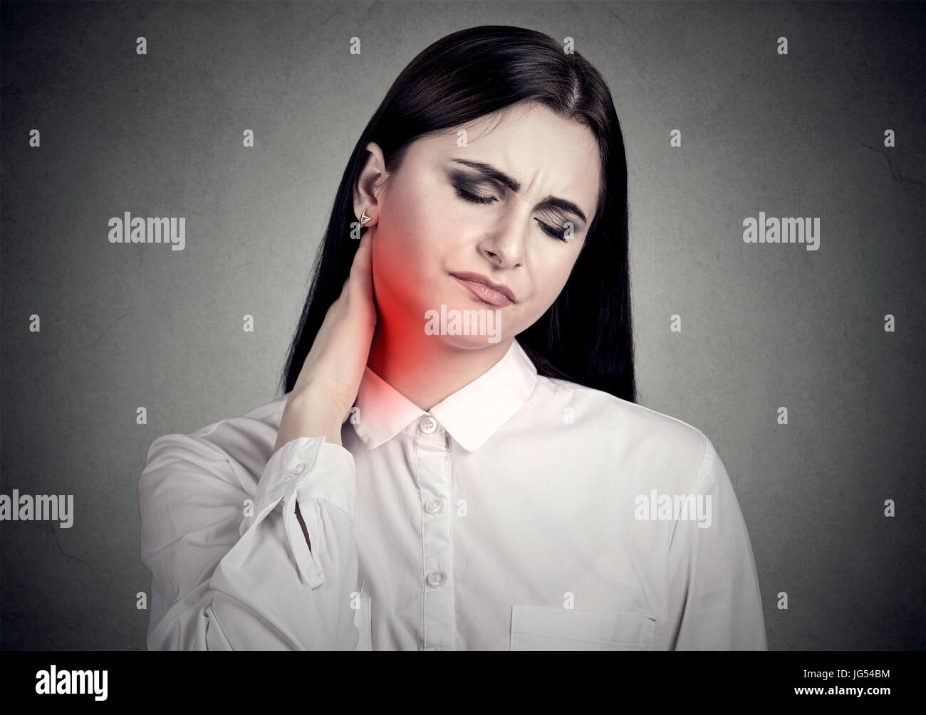 Woman massaging painful neck colored in red isolated on gray wall background. Human face expression. Stock Photo