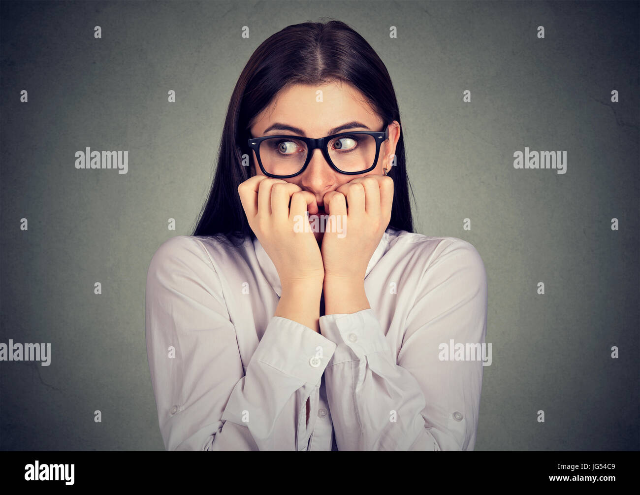Unsure anxious woman biting her fingernails craving for something isolated on gray background. Negative human emotions feelings Stock Photo