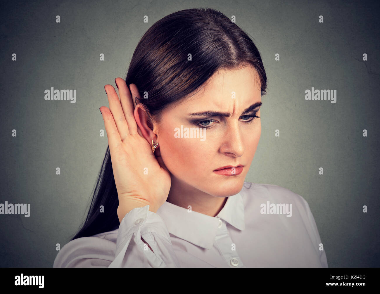 Curious woman with hand to ear carefully listening to gossip conversation isolated on gray background Stock Photo