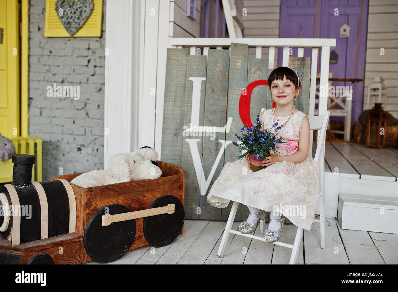 Portrait of a cute little girl in a dress sitting on a chair in a ...