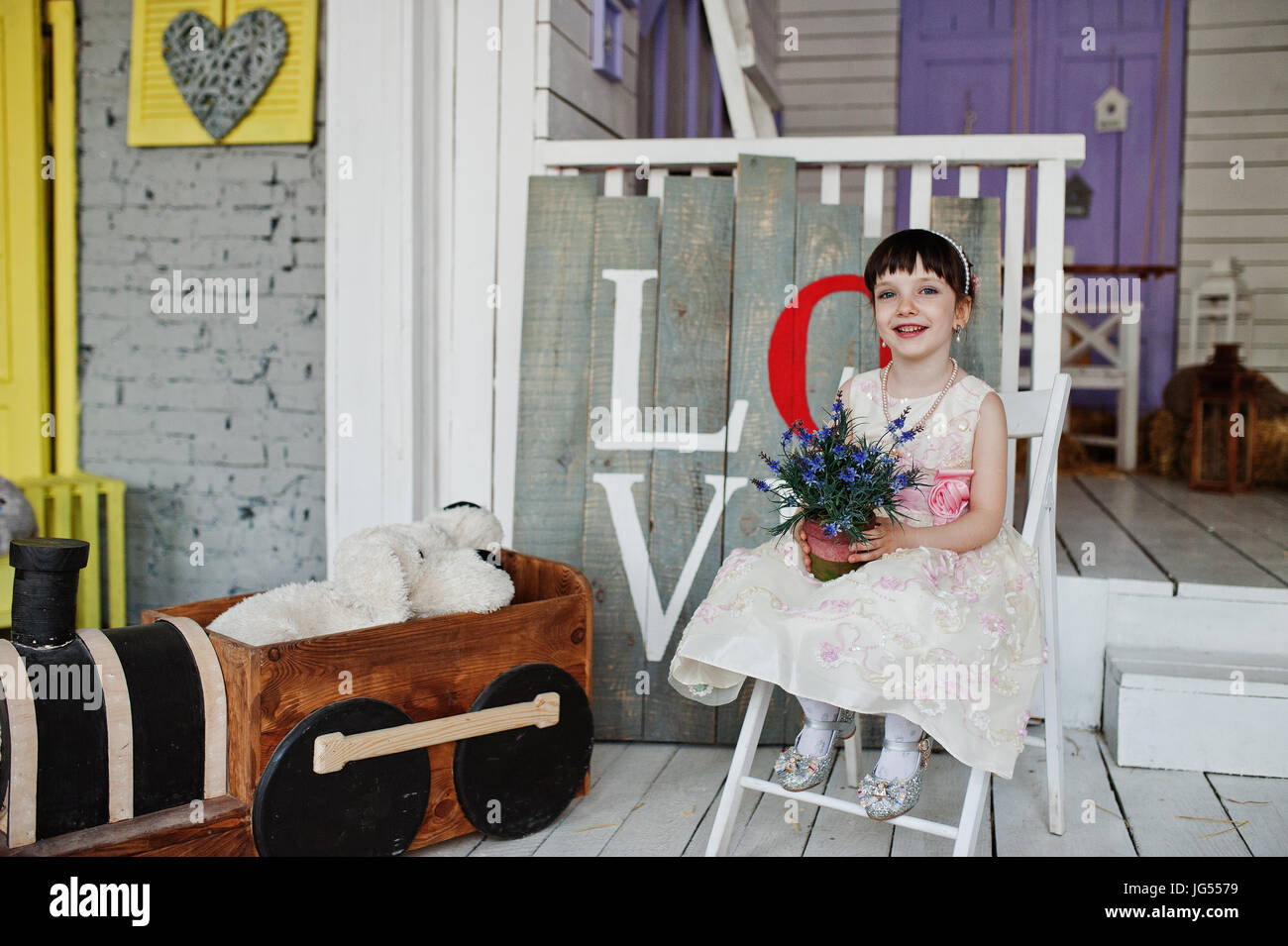 Portrait of a cute little girl in a dress sitting on a chair in a ...