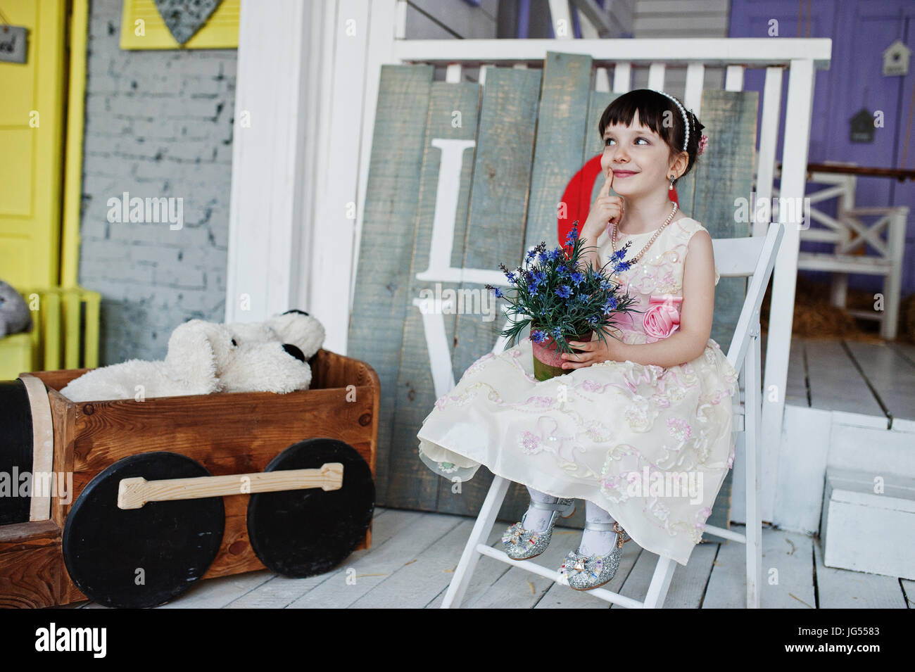 Portrait of a cute little girl in a dress sitting on a chair in a ...
