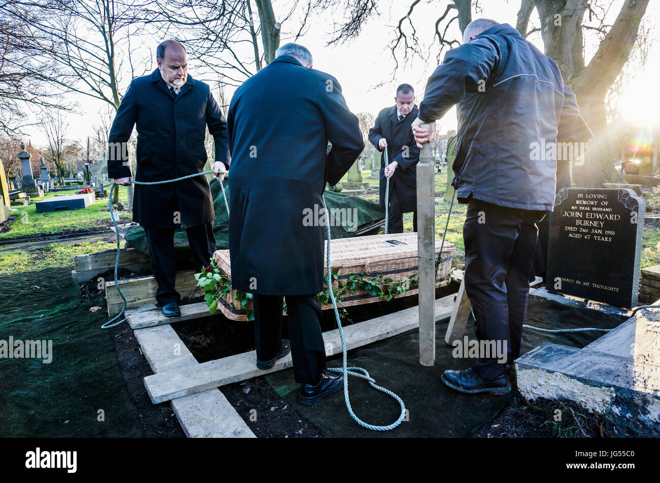A group of men supporting a wicker coffin with ropes, as it is lowered into a grave, at a cemetery in England, UK. Stock Photo