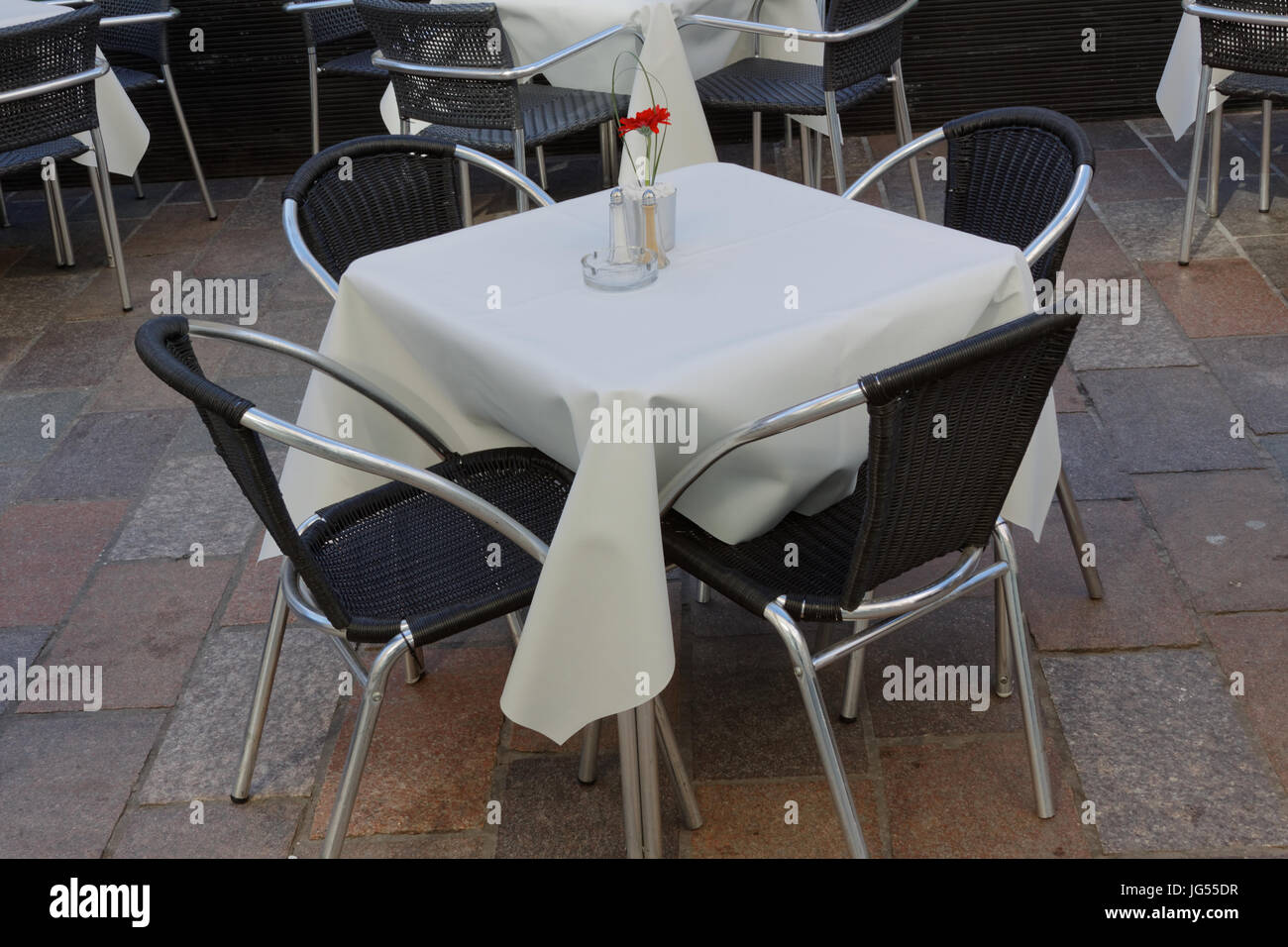 tables in a restaurant empty with white tablecloth and single romantic red rose Stock Photo