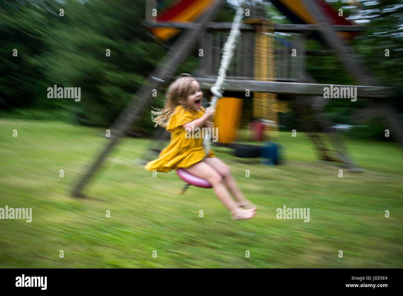 Little girl in yellow dress jumping on the trampoline Stock Photo