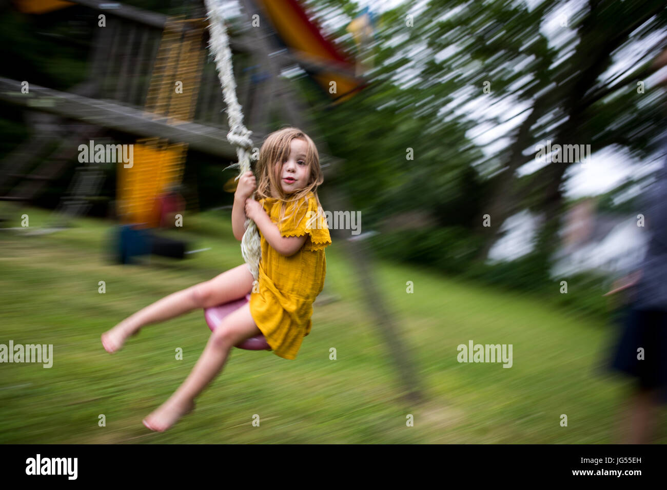 Little girl in yellow dress jumping on the trampoline Stock Photo