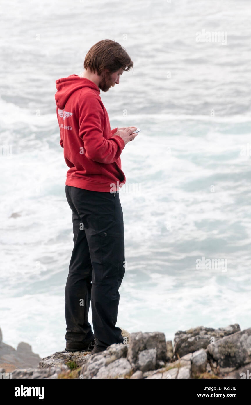Boy checking mobile 'phone on clifftop with sea in background. Stock Photo