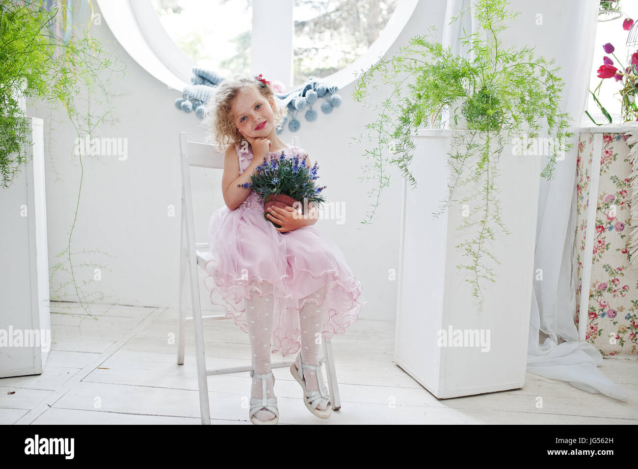 Beautiful little girl in a dress sitting on a chair with a flower pot ...