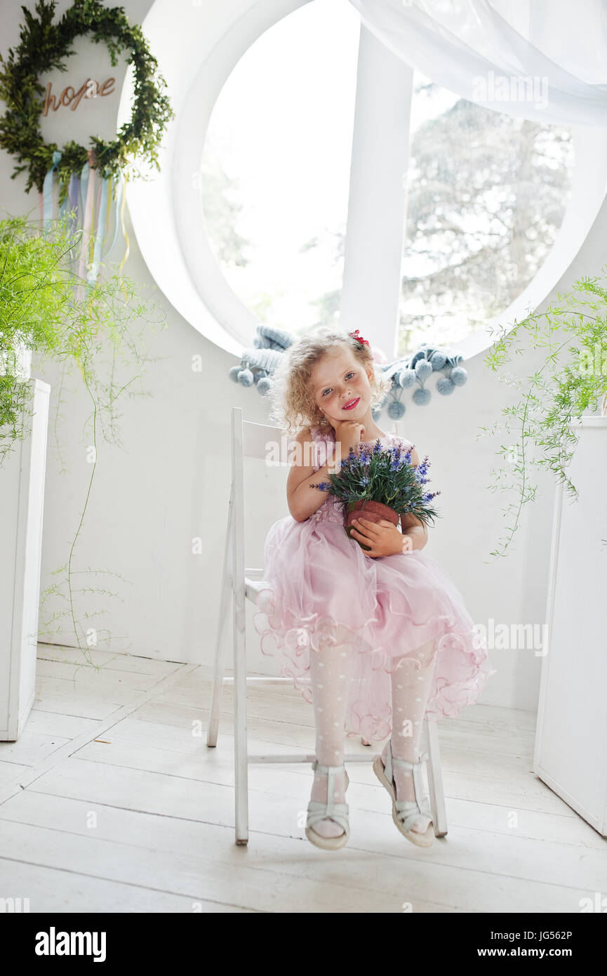 Beautiful little girl in a dress sitting on a chair with a flower pot ...