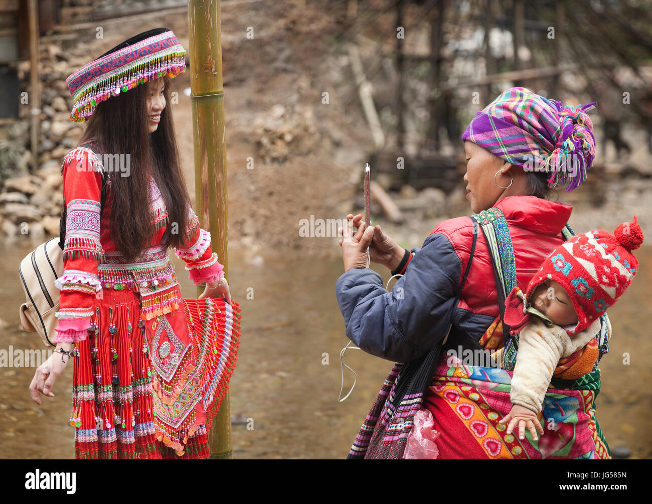 Hilltribe traditional attire, Cat Cat village at Sapa in Lao Cai, Vietnam, village member uses a smart phone to photograph her daughter Stock Photo