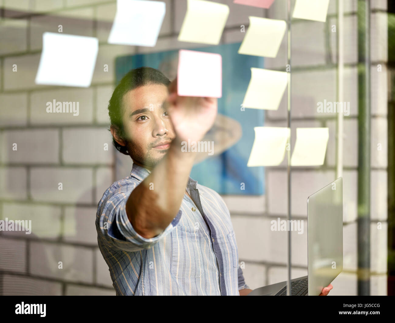 asian business man conducting an analysis in office using laptop computer and sticky notes. Stock Photo