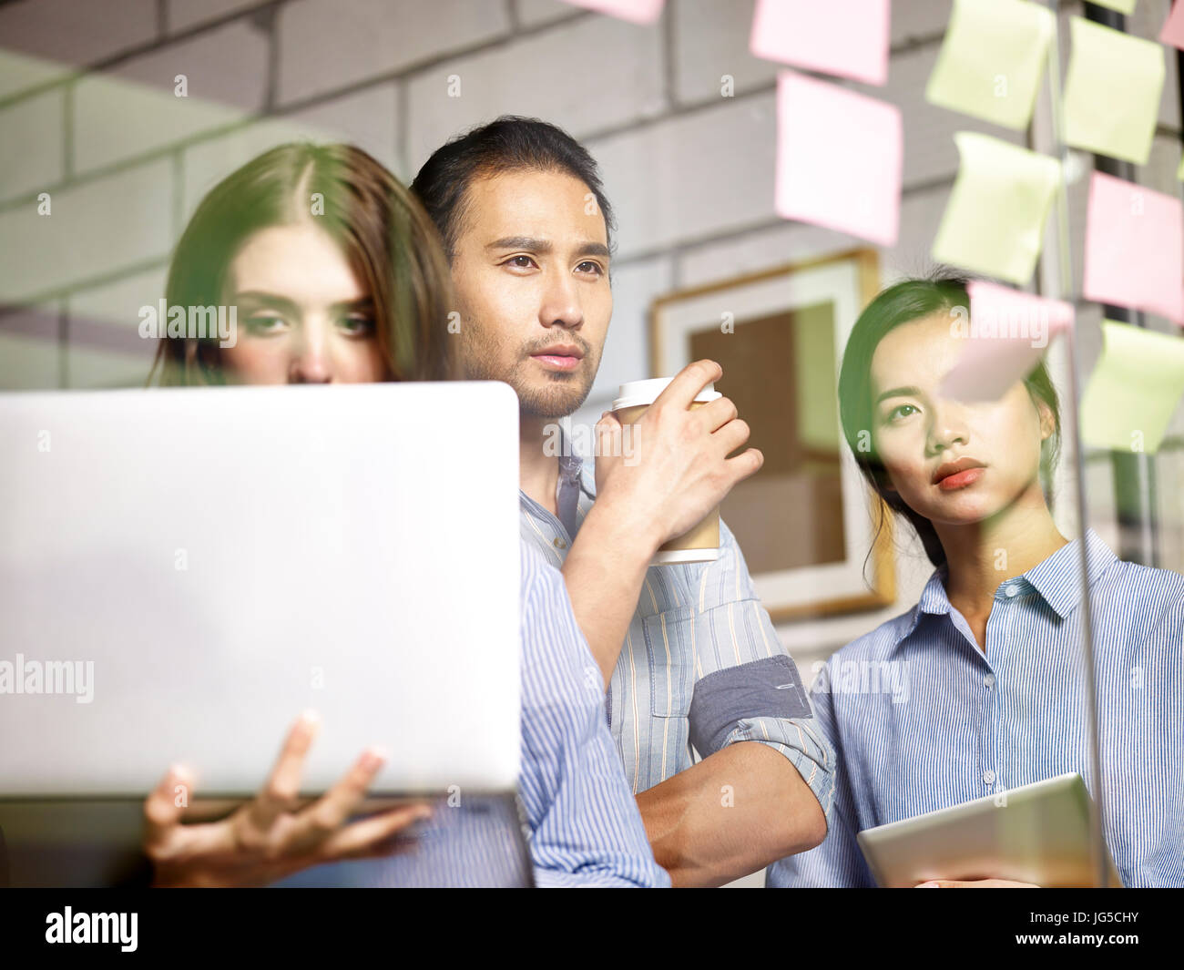 a team of asian business people conducting a SWOT analysis in office using  laptop computer and sticky notes. Stock Photo