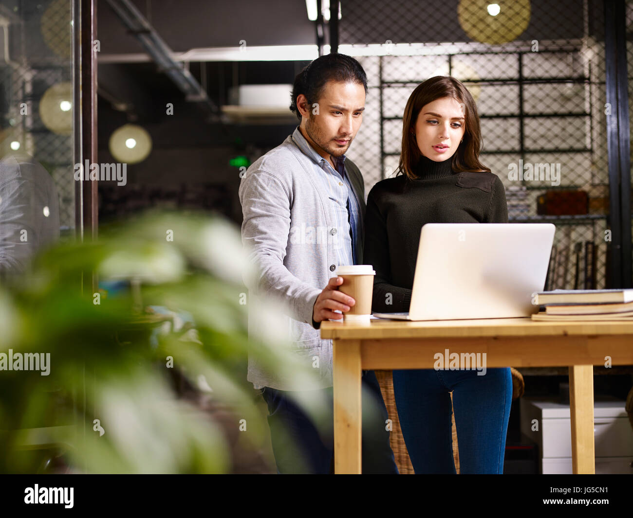 asian and caucasian employee in small private company working together using laptop computer. Stock Photo