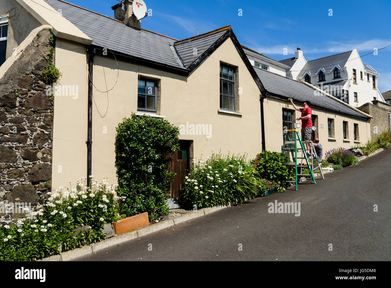 Two men painters painting a picturesque cottage on a steep hill road. Stock Photo