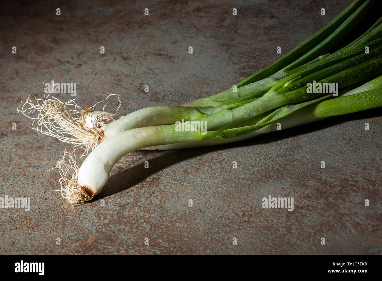 Fresh green onion stalks with water drops on ceramic hob Stock Photo