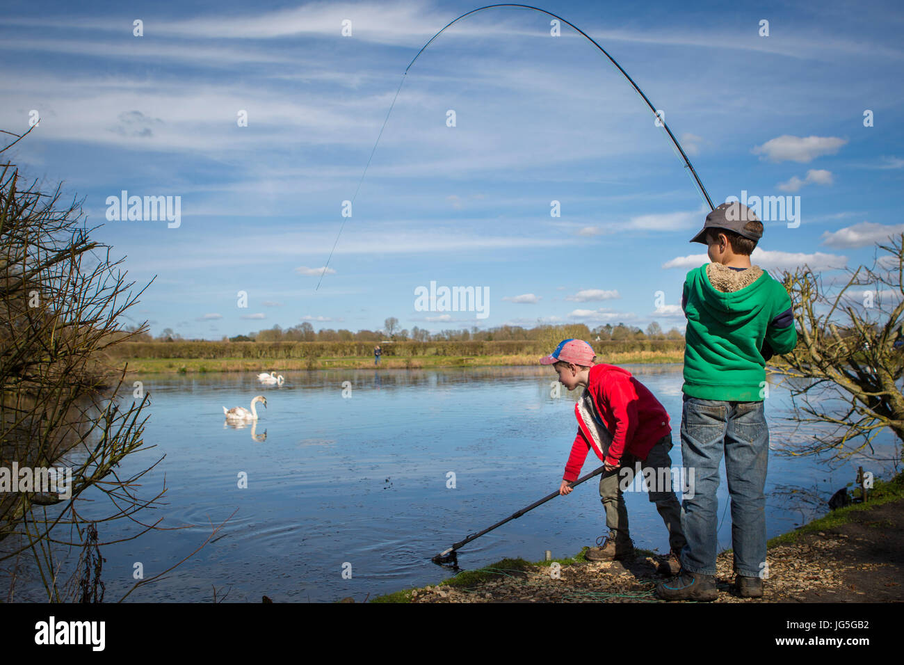 Two boys catching and netting a fish in a lake, England, UK Stock Photo