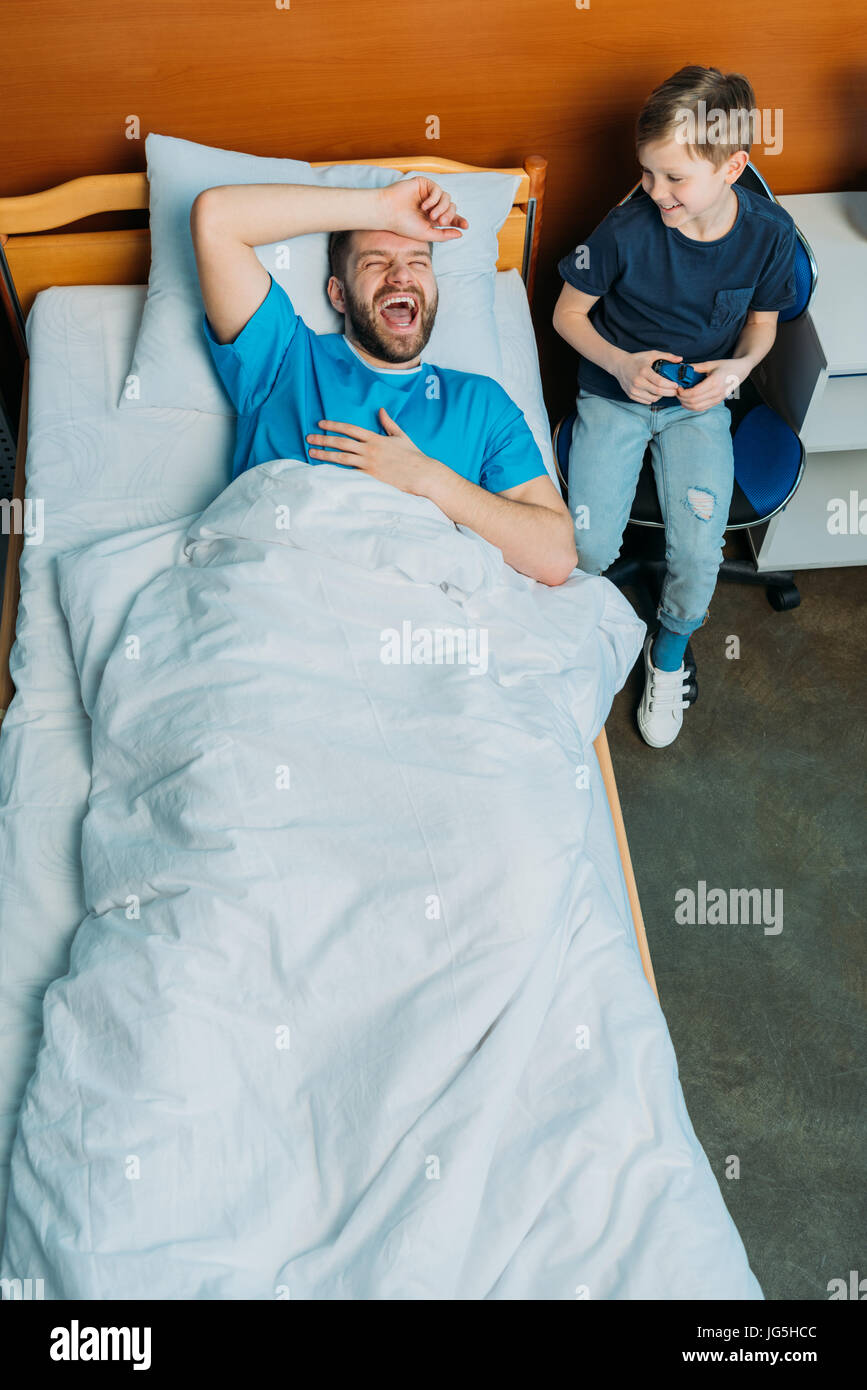 Son Sitting Near His Sick Father Laying On Hospital Bed At Ward Hospital Patient Care Stock