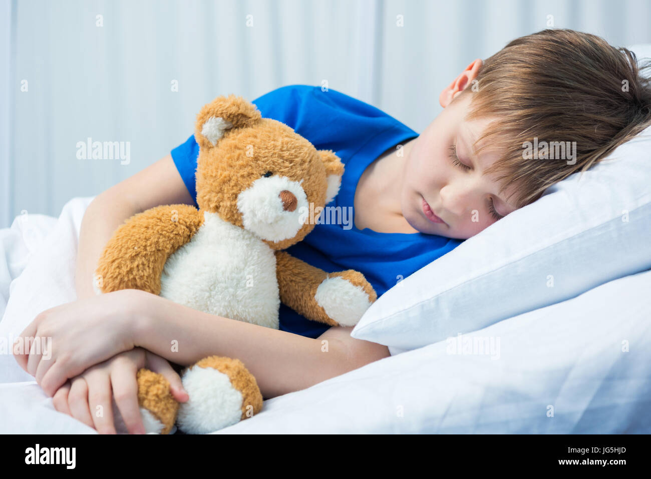 Sick little boy sleeping in hospital bed with teddy bear Stock Photo