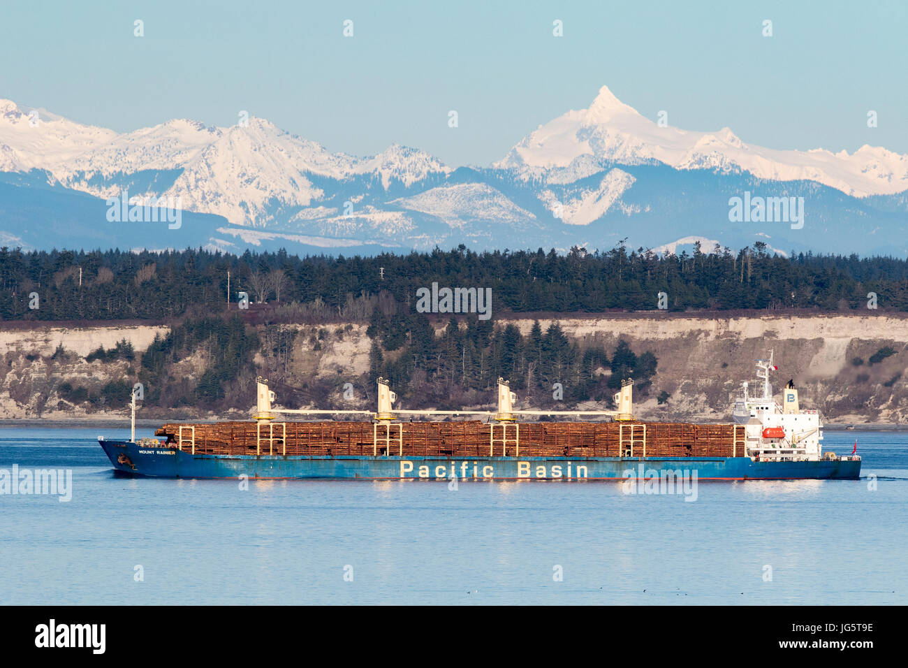 Log ship used for logging passes through Puget Sound, Washington with Cascade Mountains in background. Stock Photo
