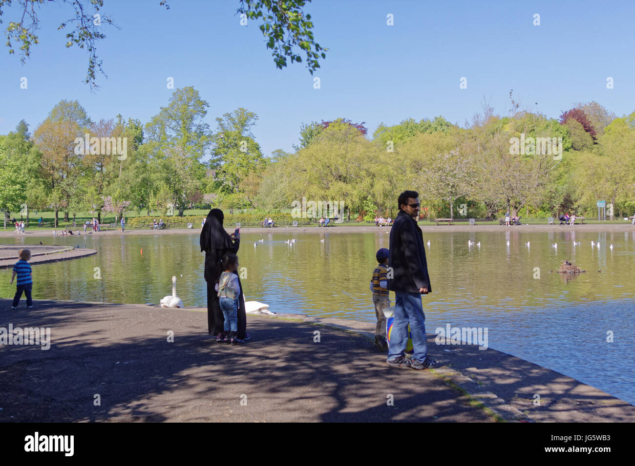 Asian family refugee mother father  dressed Hijab scarf near pond  in the UK everyday scene mother and child in Queens Park Glasgow Stock Photo