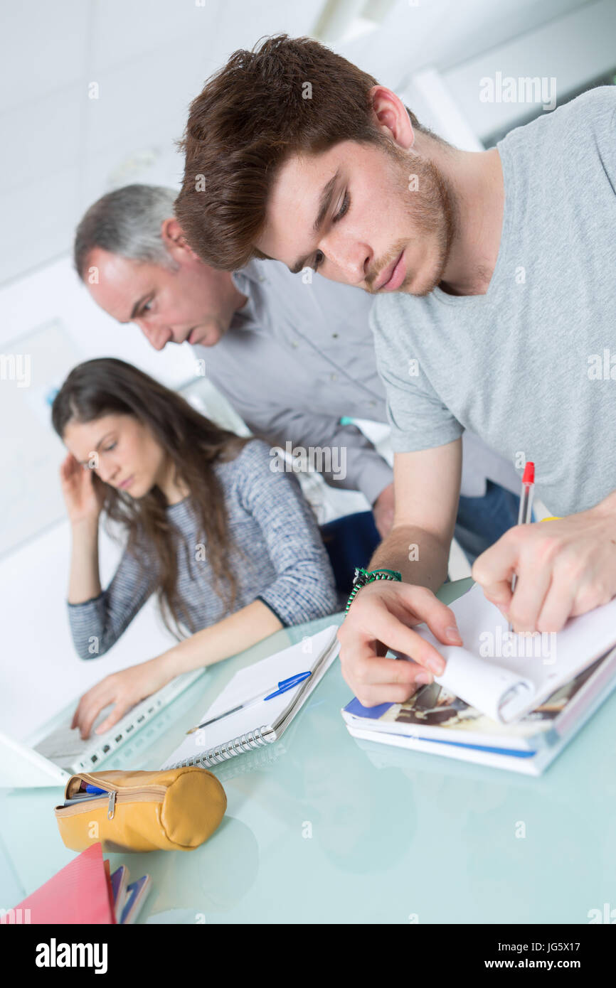 2 attentive adult students with male teacher in classroom Stock Photo