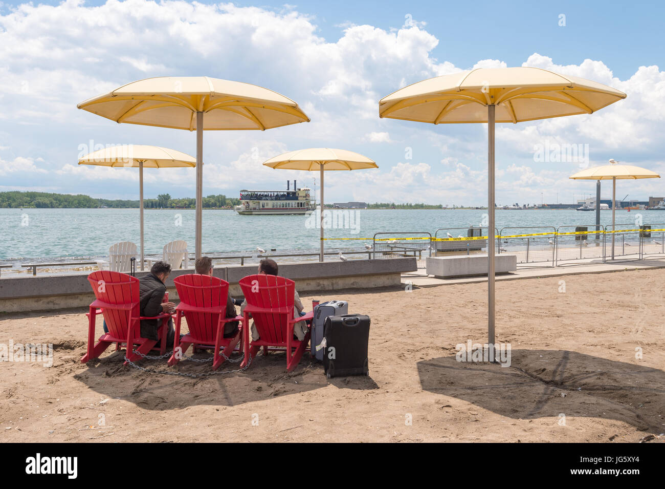 Toronto, Canada - 26 June 2017: Three men sitting next to travel backs on Toronto Beach and looking at Ontario Lake Stock Photo