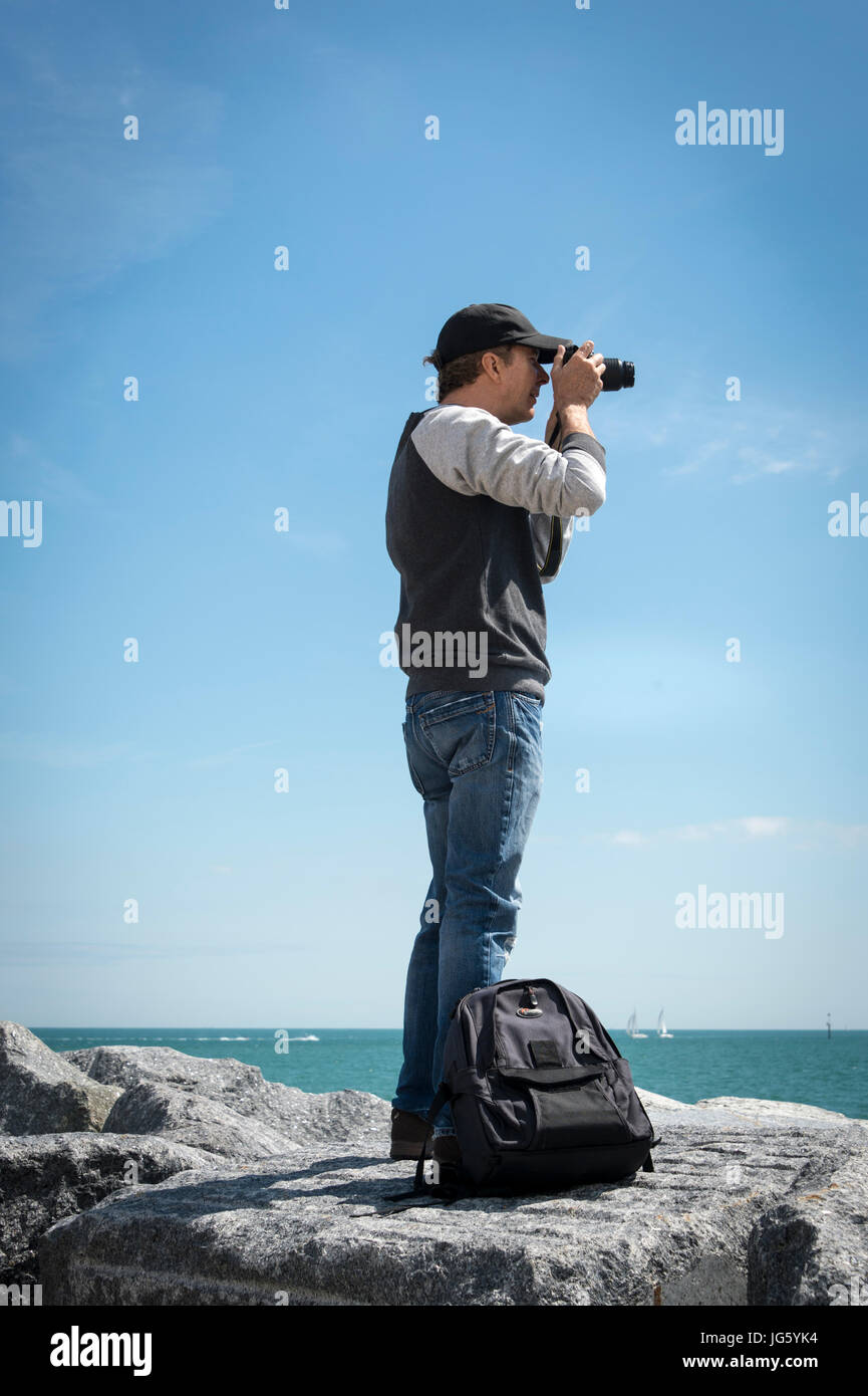 man with a camera on top of rocks by the coast Stock Photo