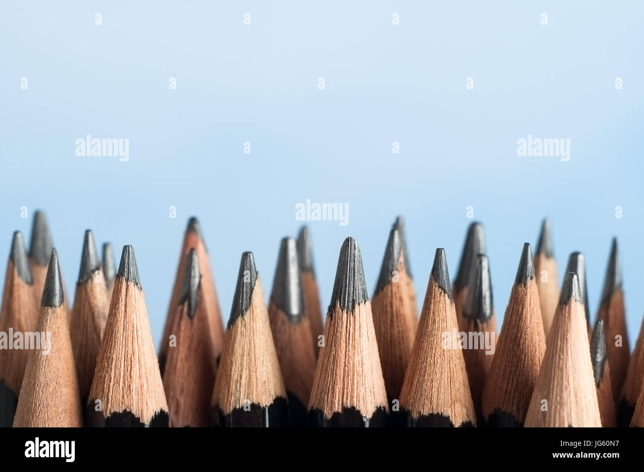 An uneven row of mixed graphite pencils, standing upright against a sky blue background with their tips pointing upwards from the bottom half of the f Stock Photo