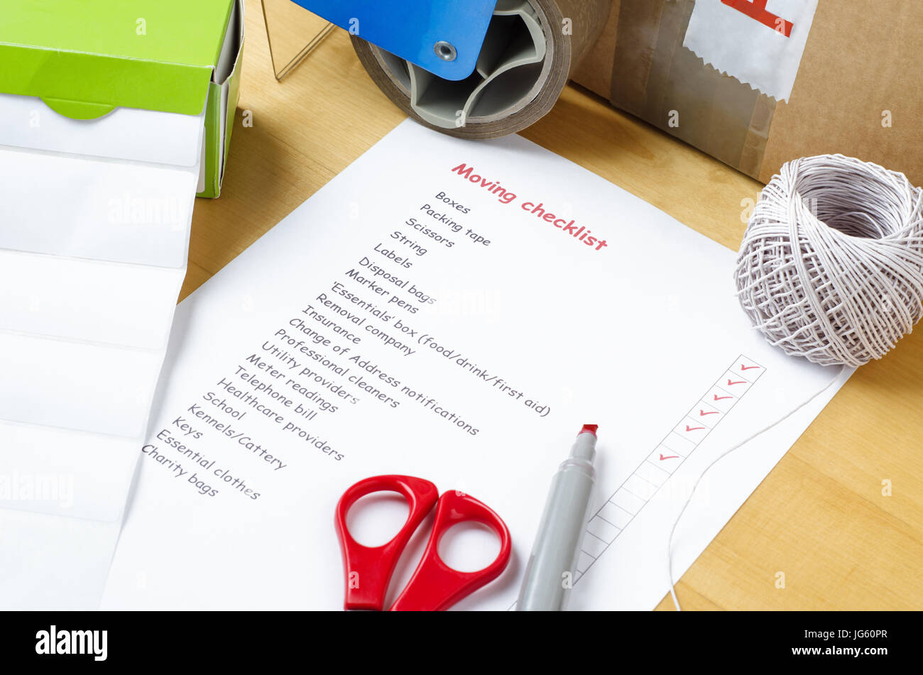 A house moving checklist on a table, surrounded by labels, packaging tape roller, scissors, red marker pen, a ball of string and a sealed box.  Some o Stock Photo