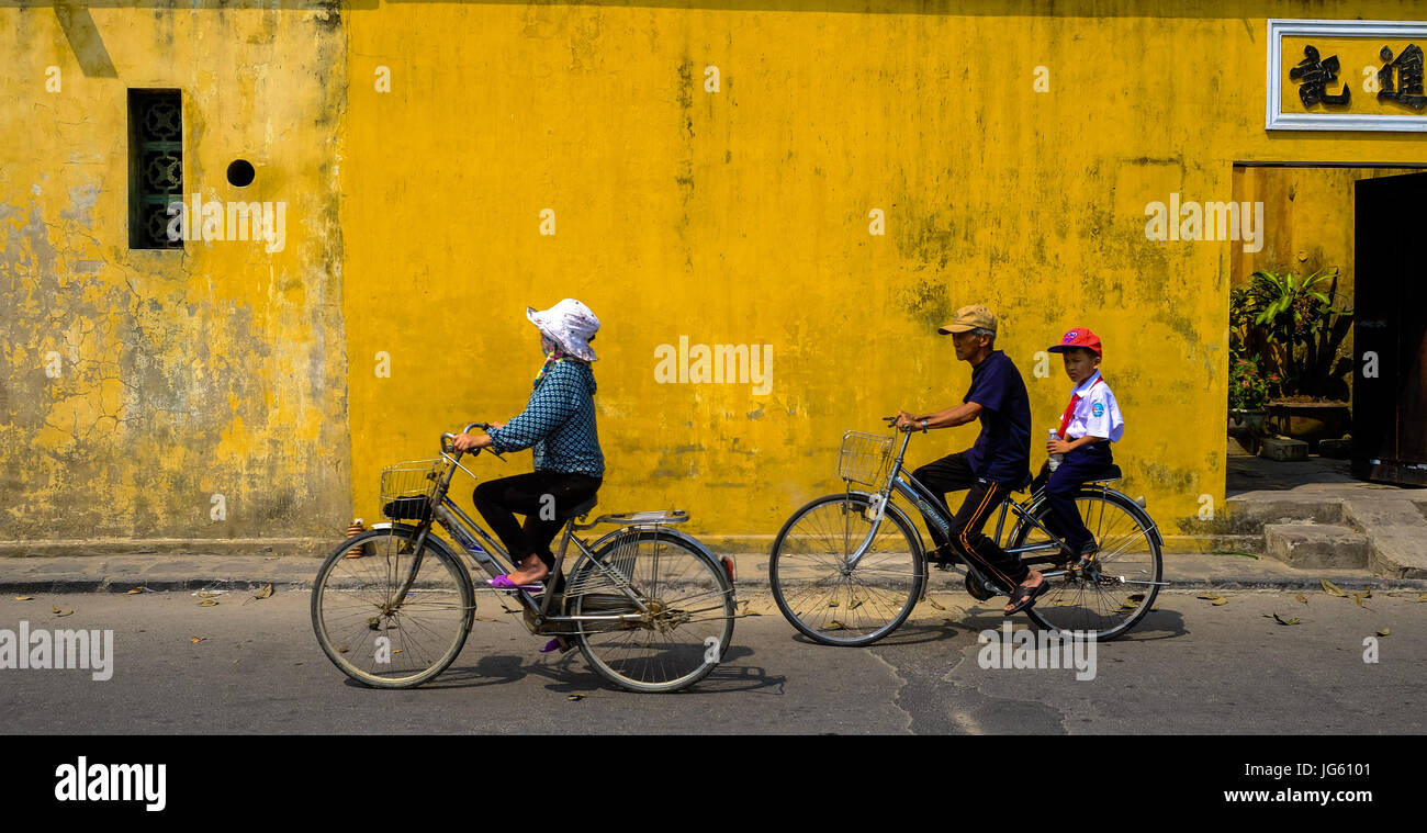 A Vietnamese woman rides a bike in a street in Hoi An, Vietnam Stock Photo